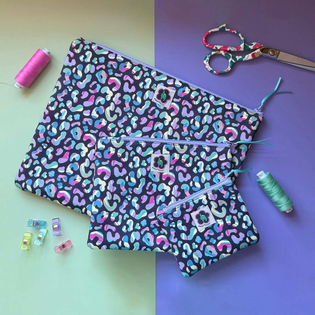 Three matching colourful leopard print zip pouches arranged with scissors, pink and mint thread, and sewing clips.
