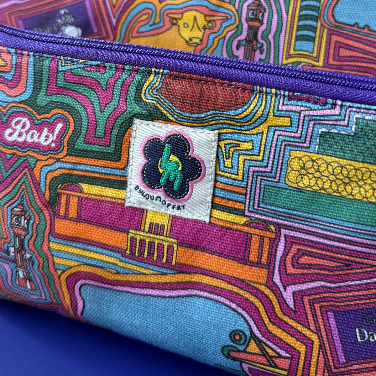 Close-up of a floral zip pouch with two matching bags, featuring a colourful retro pattern with a light purple zipper and a visible ByLouMoffat brand label.