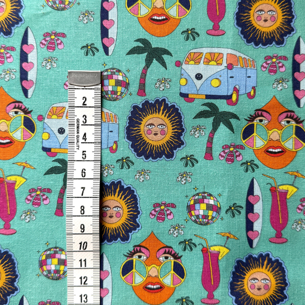 Mint green hippie fabric beside a centimetre tape measure to show the scale of the campervan, sunshine and peace-sign motifs.