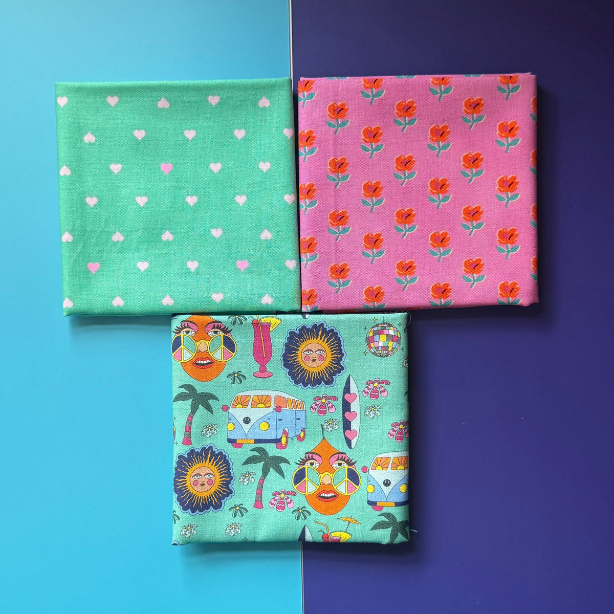 Three folded hippie, floral and heart-print fat quarters arranged in a triangle on a turquoise and navy background.