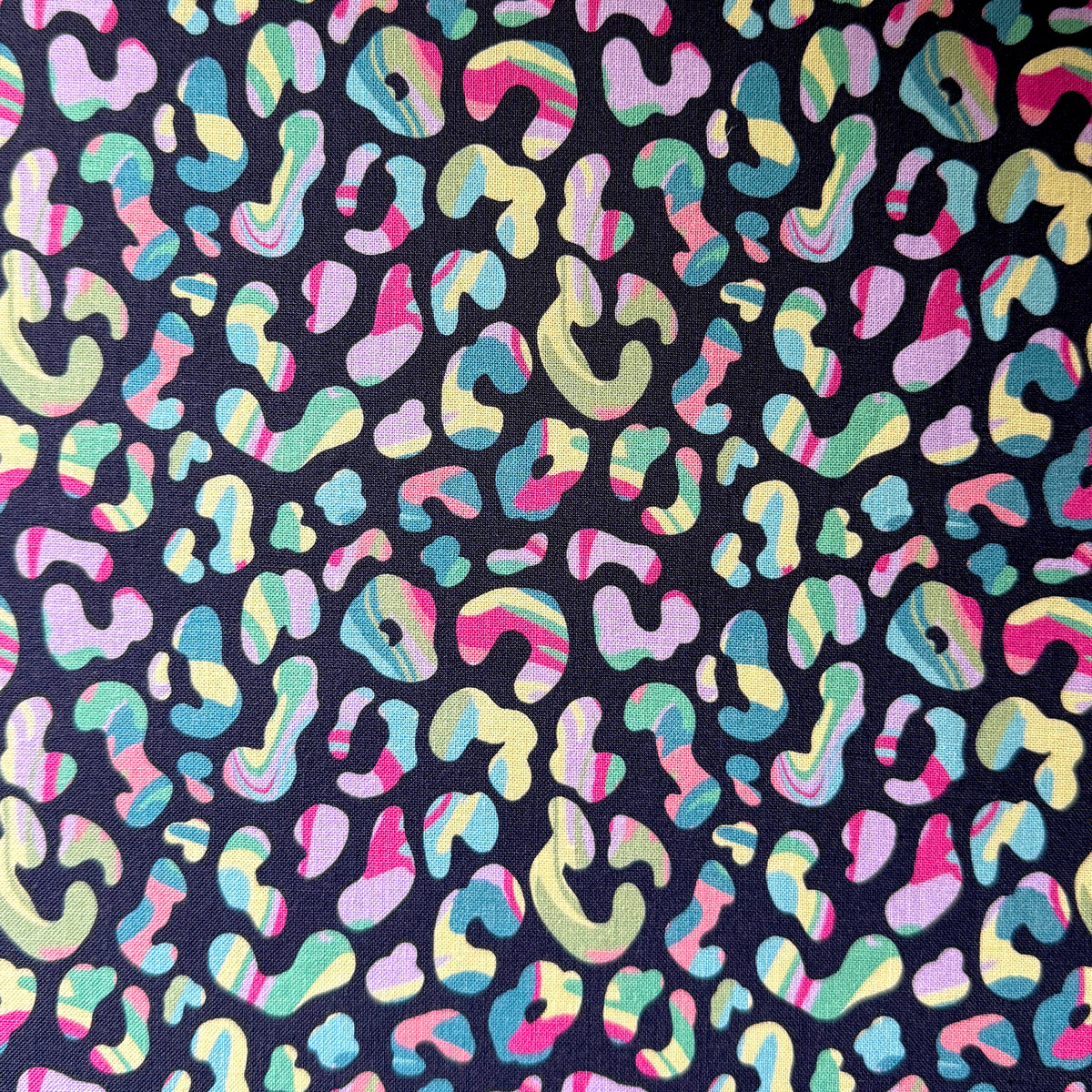 Leopard print fabric laid flat, showing multicoloured spots with striped and swirled details on a dark navy background.
