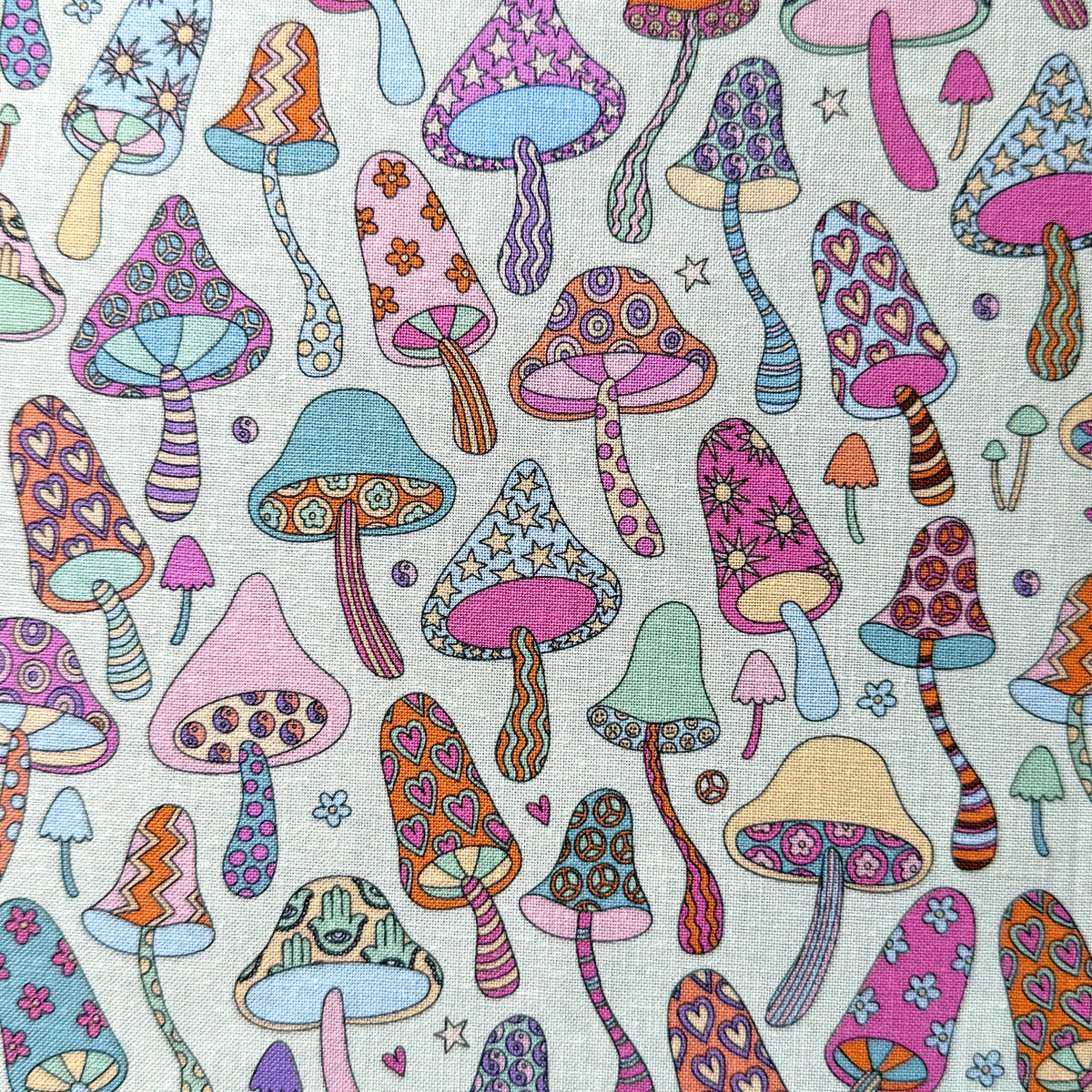 Colourful mushroom fabric laid flat, with hearts, stars, flowers, stripes and peace signs decorating the mushrooms on a pale mint green background.