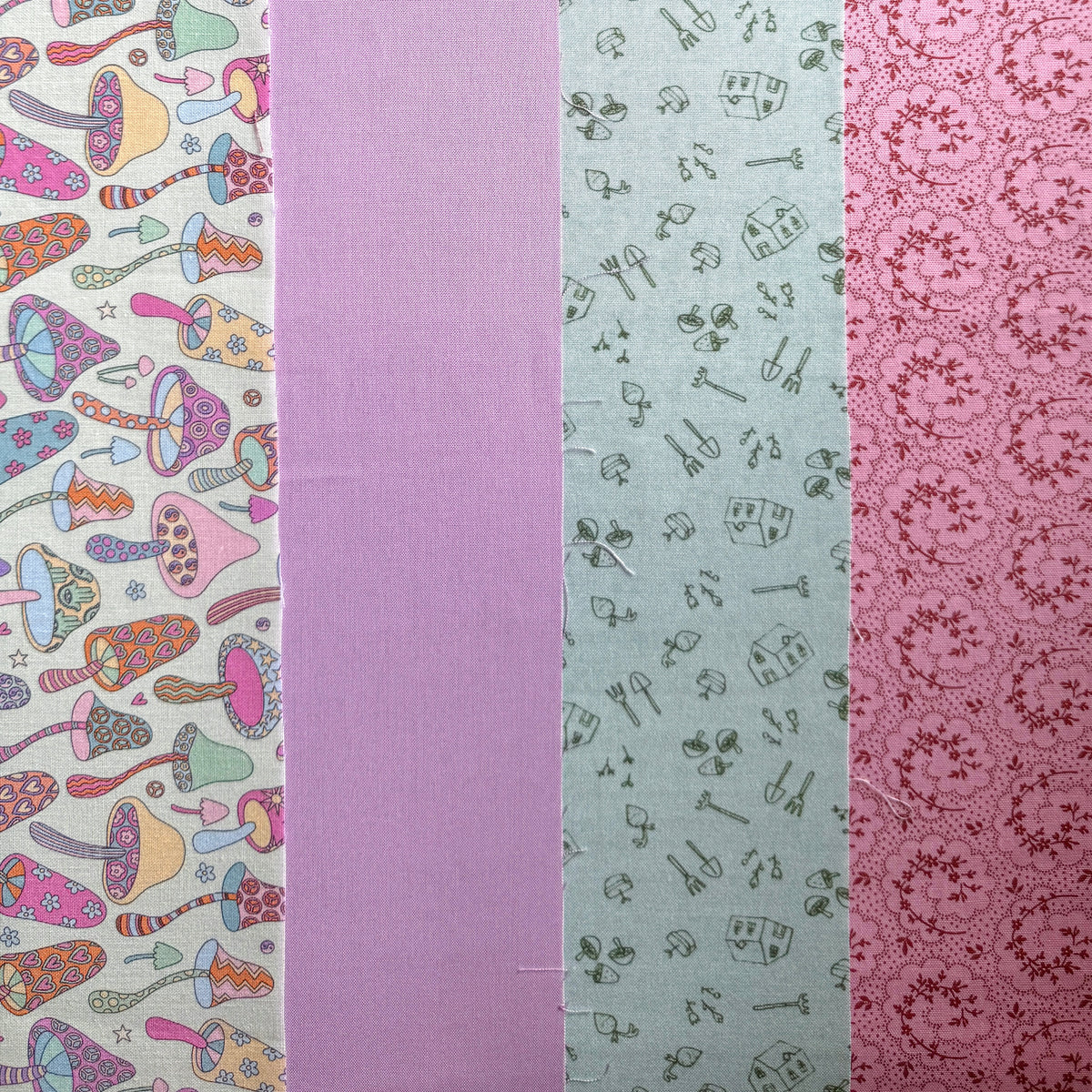 Four fabrics laid side by side: colourful mushroom print, plain lilac, sage green gardening print and pink floral print.