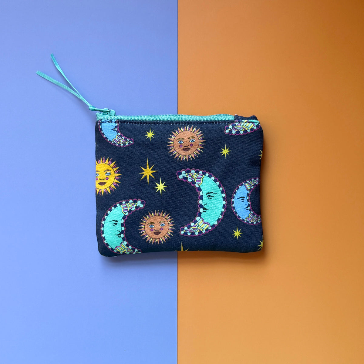 Back of the small navy pouch, showing colourful suns, crescent moons and stars with a turquoise zip.