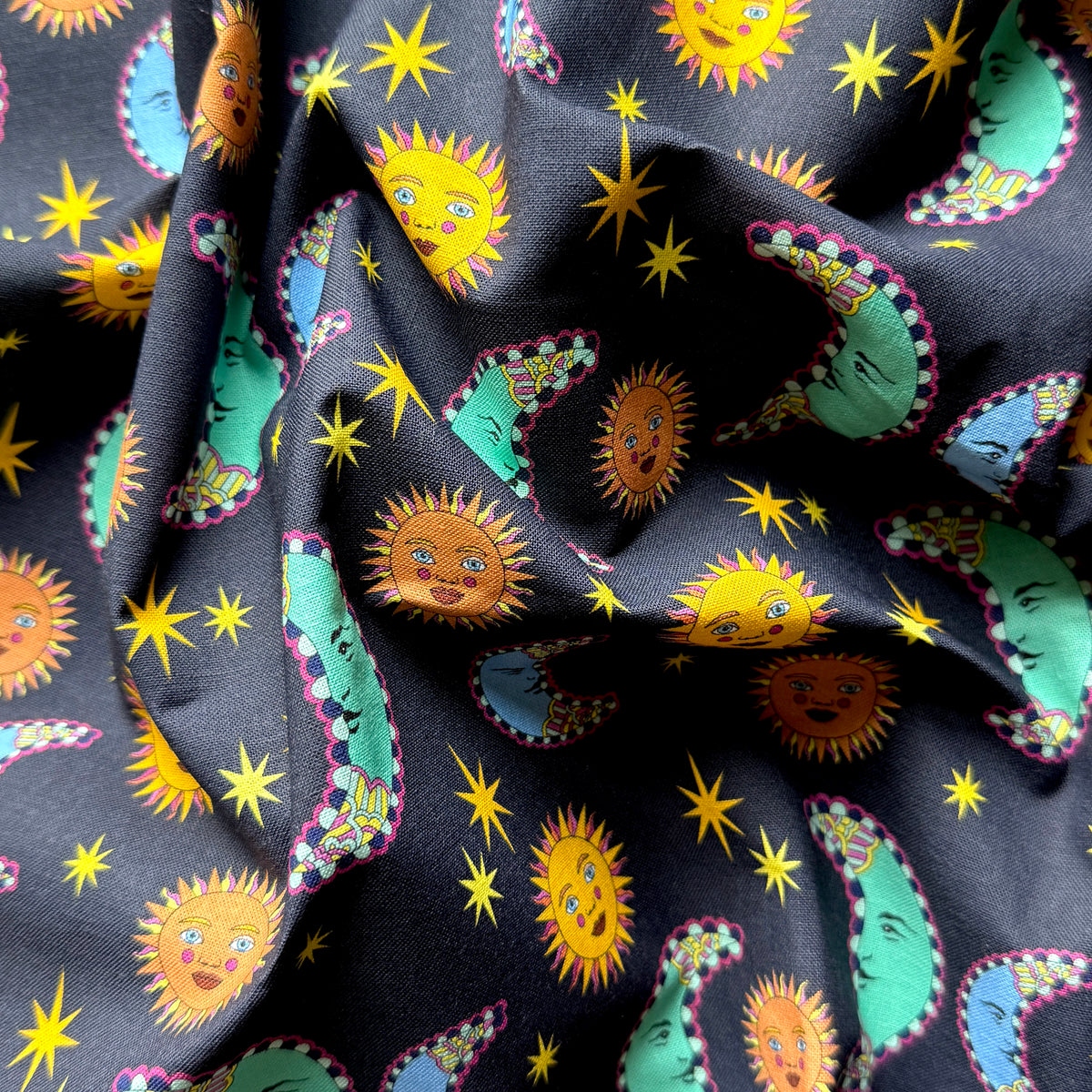 Draped sun and moon fabric showing its texture and colourful celestial faces and stars on a navy background.