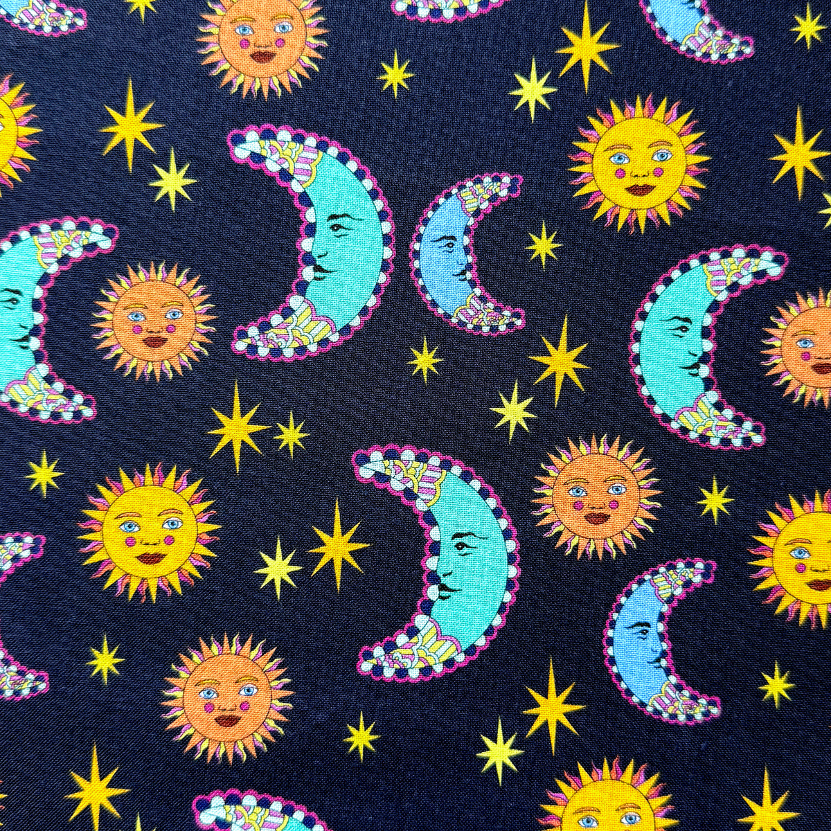 Navy celestial fabric laid flat, featuring golden sun faces, turquoise and blue crescent moons with pink outlines, and yellow stars.
