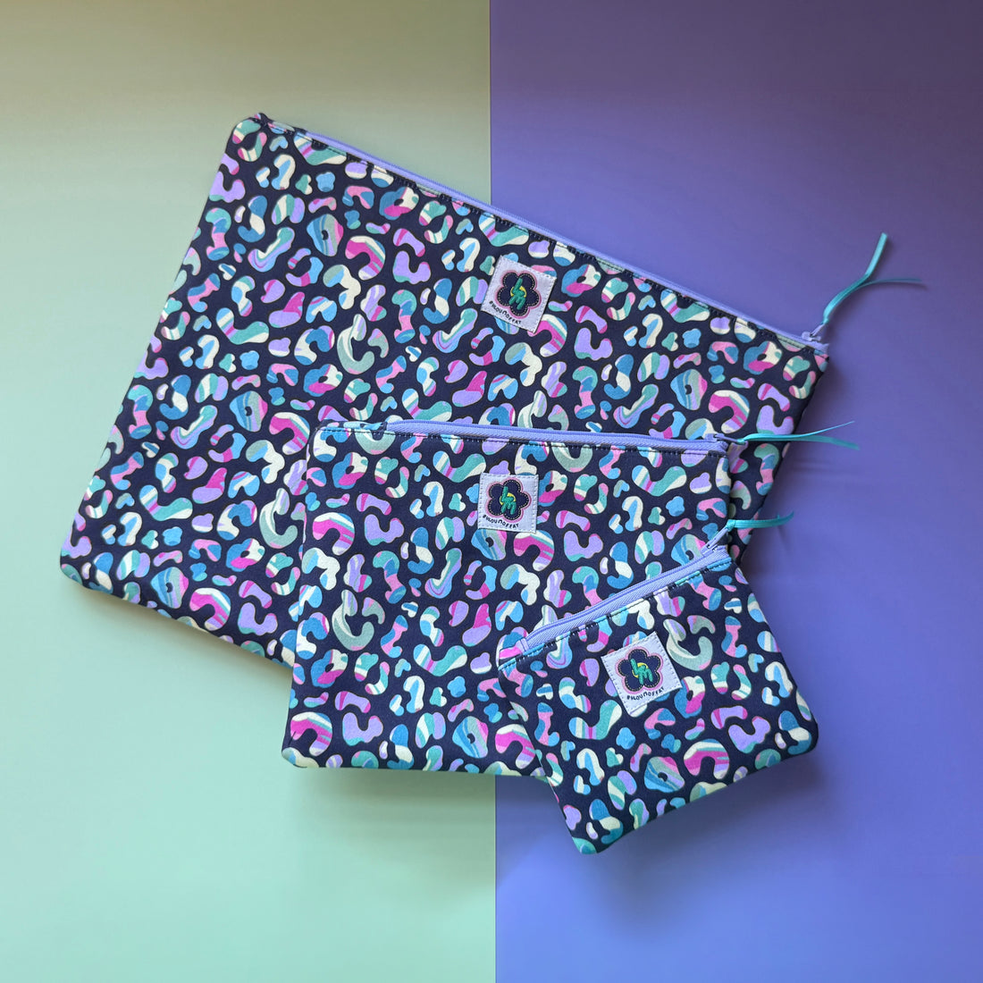 Three leopard-print zip pouches in small, medium and large, with multicoloured spots on a dark background. 