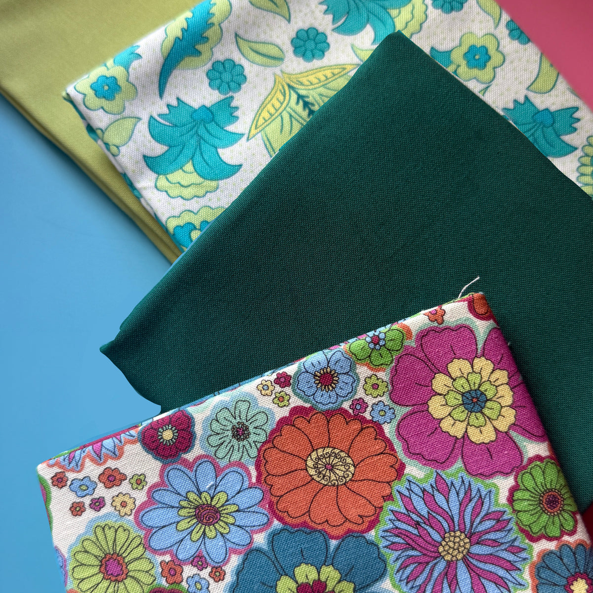 Close-up of the floral fat quarter bundle showing colourful flower prints, plain teal and lime fabrics, and fabric texture.