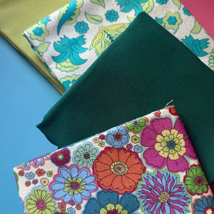 Close-up of the floral fat quarter bundle showing colourful flower prints, plain teal and lime fabrics, and fabric texture.