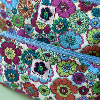 Close-up of a floral zip pouch with two matching bags, featuring a colourful retro flower pattern on a cream background with a light blue zipper and a visible ByLouMoffat brand label.
