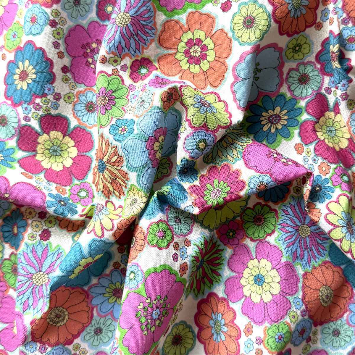 Draped retro floral fabric showing the fabric texture and a mix of bold blooms and tiny colourful flowers.