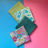 Four folded fat quarters arranged diagonally, with multicoloured retro florals, teal and lime floral print, plain teal and plain lime.