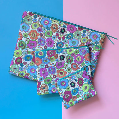 Three zip pouches in small, medium and large, with colourful 60s-style flowers and teal zips.