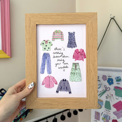 Hand holding a wooden-framed print with the words ‘There’s nothing better than sewing your own wardrobe’, surrounded by illustrated clothes in pink, green and purple.
