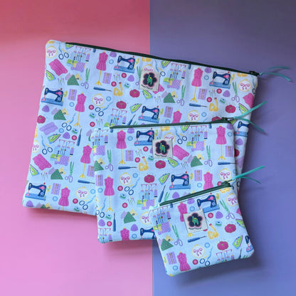 Small, medium and large sewing-print zip pouches with colourful sewing machines, scissors, dressmaking mannequins, embroidery hoops, unpickers and other sewing notions. Fabric is bright and colourful with a light blue background. 