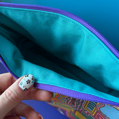 Close-up of a zippered pouch opened by a hand with black-and-white floral nail art, showing a turquoise water repellant interior and a multicolor exterior.