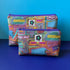 Two fabric zip pouches with a colourful  retro inspired Birmingham based print, ByLouMoffat floral logo labels in the top middle of each bag and purple zip with a teal ribbon pull. Displayed on a royal blue surface against a light blue background.