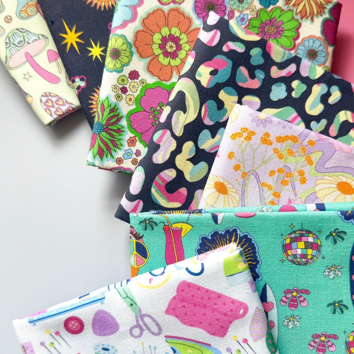 Close-up of overlapping fat quarters, showing the fabric texture and colourful floral, leopard, mushroom, celestial, hippie and sewing prints.