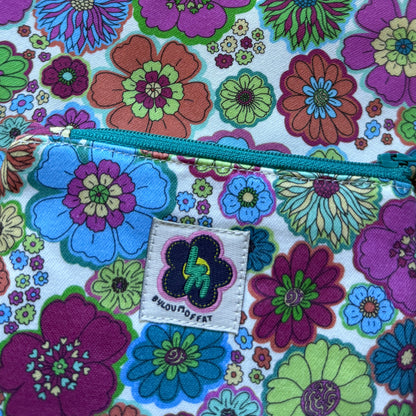 Close-up of the colourful 60s floral fabric that features retro inspired flowers. The bag has a teal zip and stitched ByLouMoffat label.

