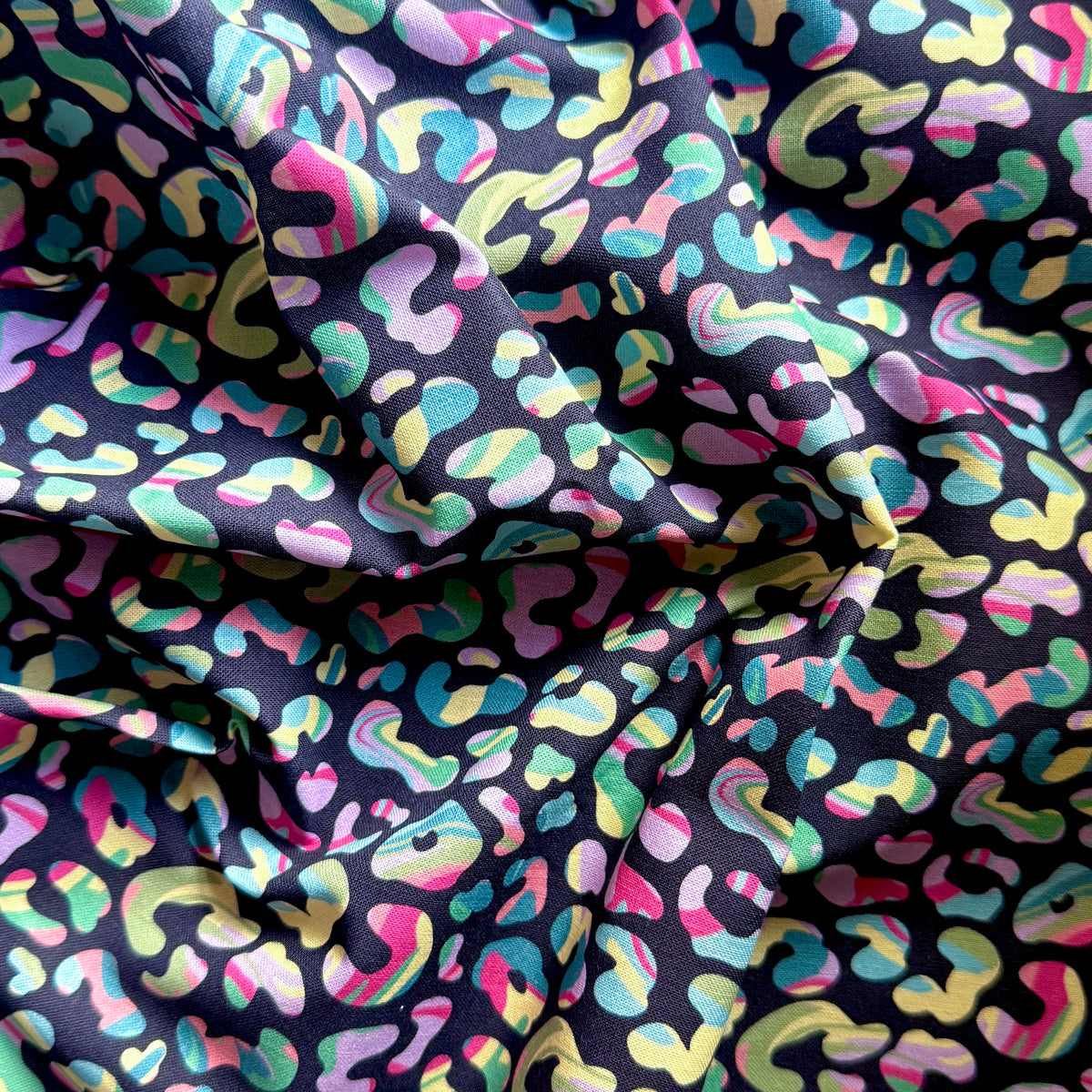 Draped leopard print fabric with pink, lilac, mint, turquoise and pale yellow spots on a dark background.