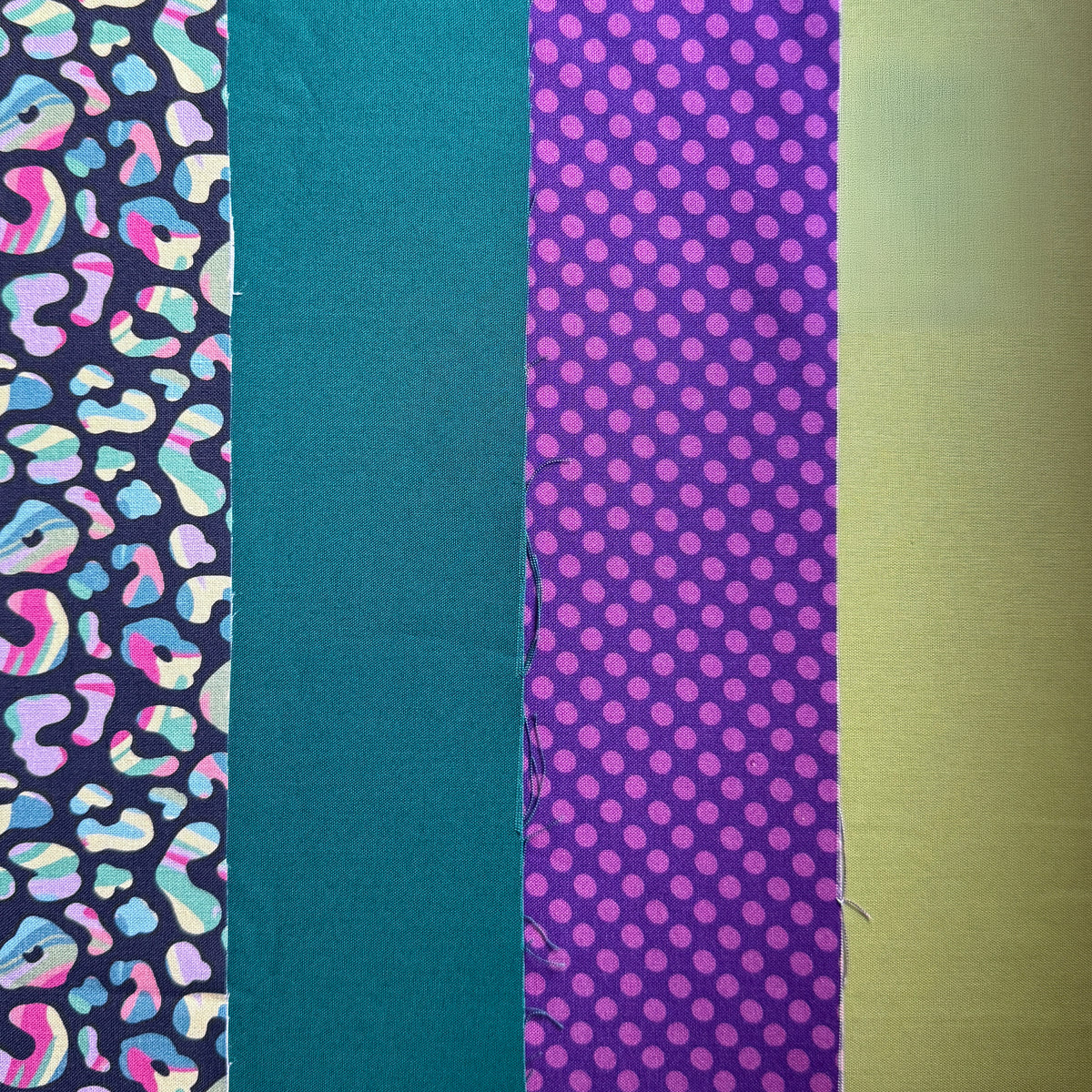 Four fabrics laid side by side: colourful leopard spots on navy, plain teal, purple polka dots and lime green.