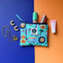 Small turquoise Hippie Pouch with campervan, disco ball, palm tree and surfboard and peace-sign print, shown with cosmetics and gold jewellery.