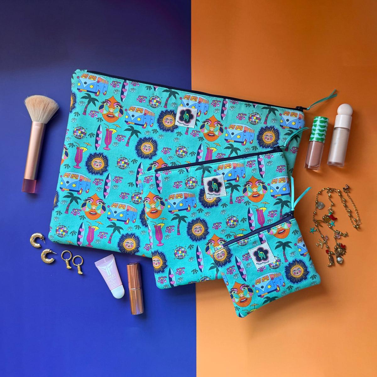 Small, medium and large turquoise Hippie Pouches arranged with cosmetics, a makeup brush and gold jewellery.