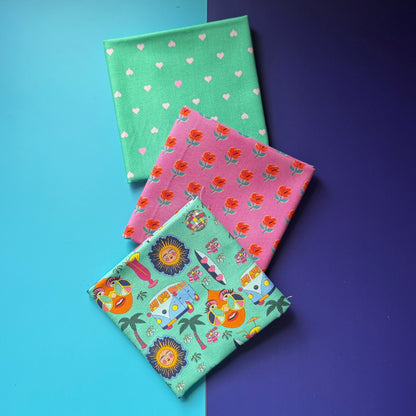  Three folded fat quarters fanned out, featuring tiny hearts on mint green, orange flowers on pink and a colourful hippie print that features suns, campervans, palm trees, disco balls, cocktail glasses and a girl with peace sign sunglasses. 