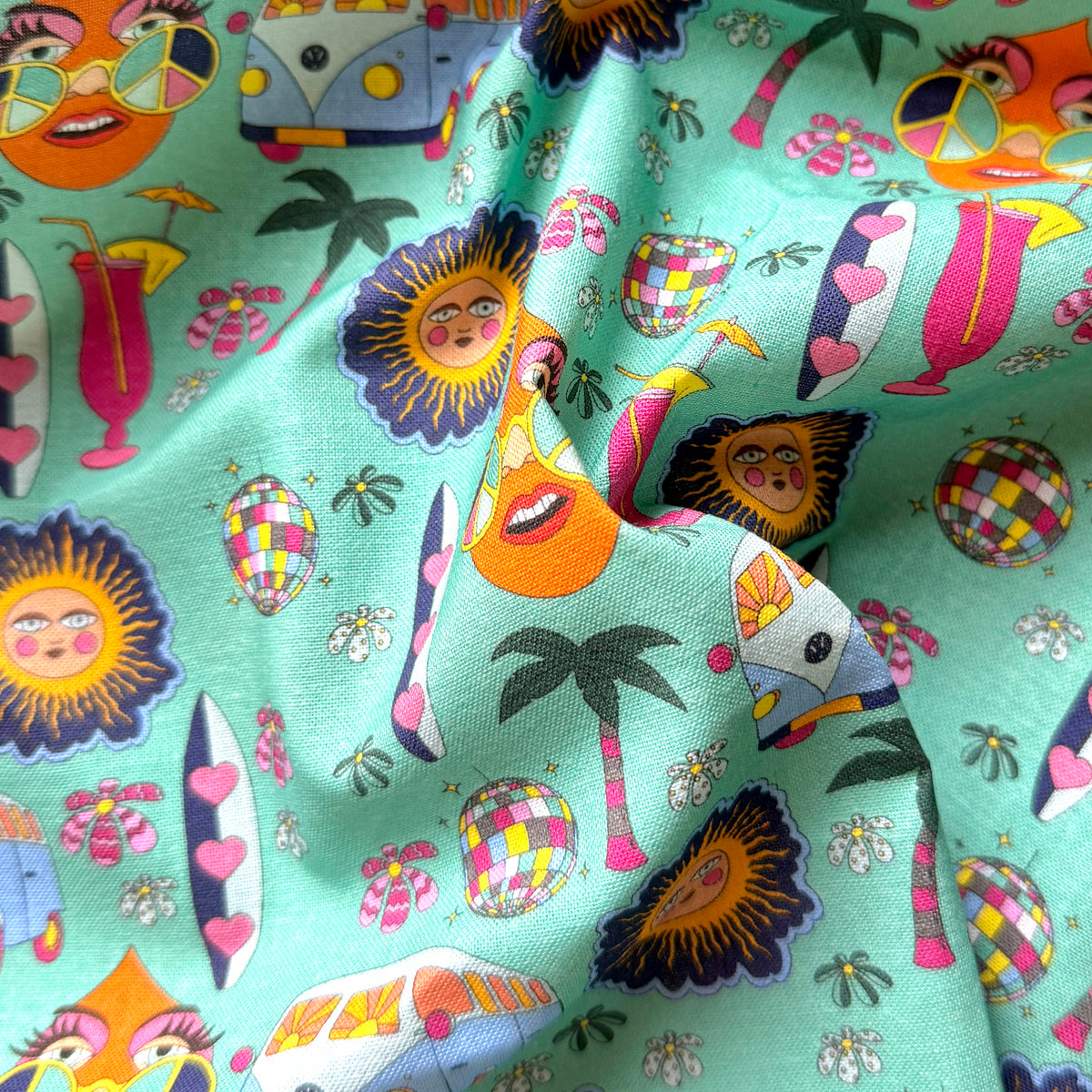 Draped hippie print fabric showing its texture and colourful retro holiday motifs on a mint green background.
