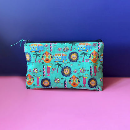 A rectangular zippered pouch with a colourful vintage inspired hippie print with teal background sits on a pink surface against a royal blue backdrop. The pouch features a dense pattern of camper vans, surf boards, cocktails, sun, palm tress and disco ball. on a teal base, with a navy zipper.