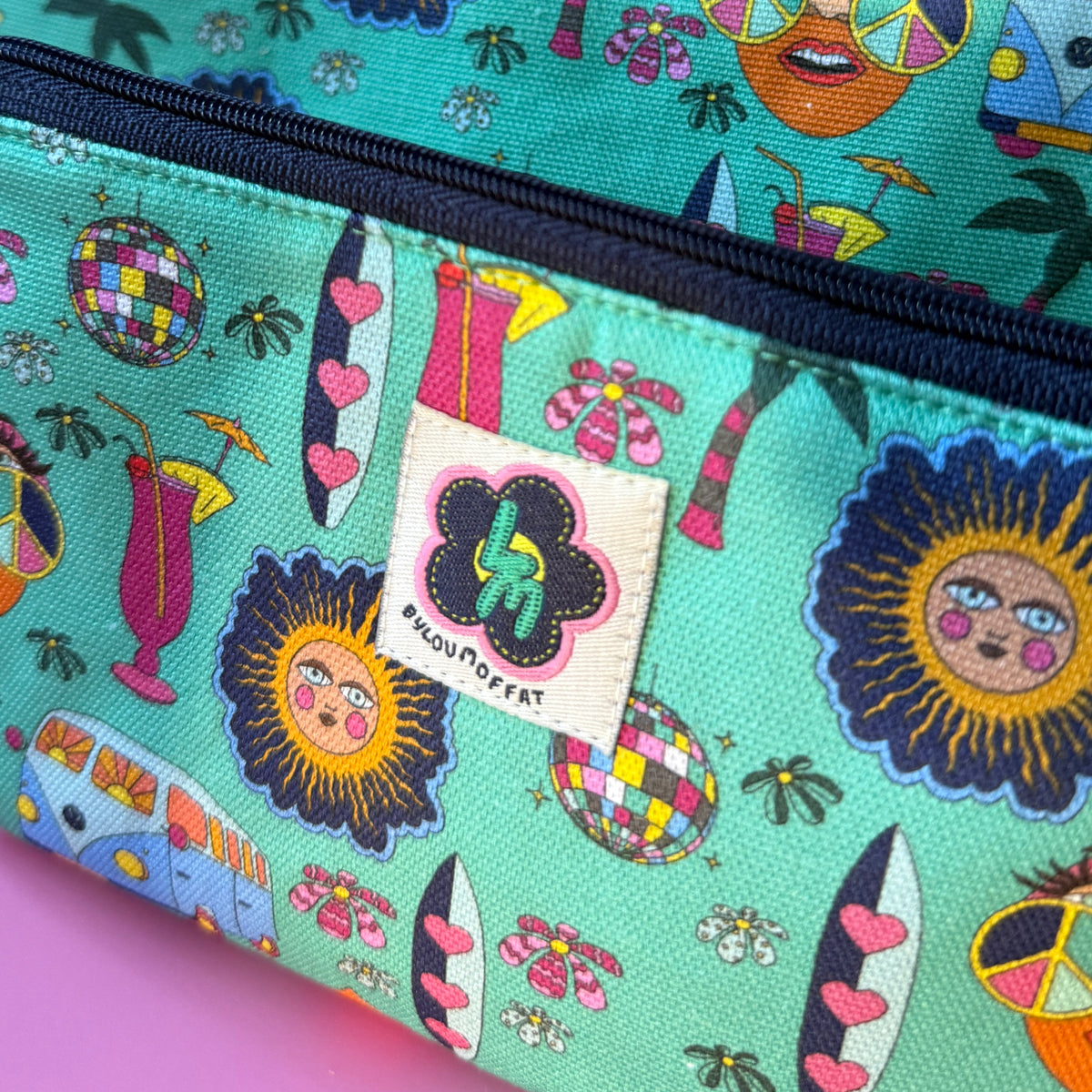 Close-up of a hippie zip pouch with two matching bags, featuring a colourful retro pattern on a teal background with a navy zipper and a visible ByLouMoffat brand label.