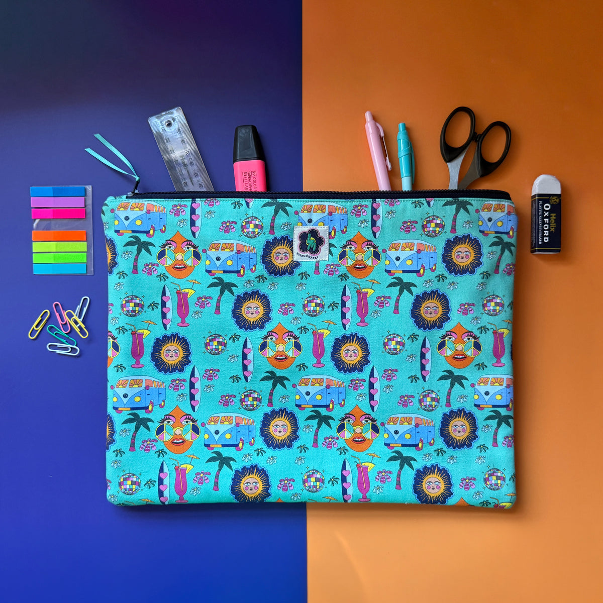 Large turquoise Hippie Pouch with retro print, shown with pens, a ruler, scissors and other stationery. The fabric a colourful retro design featuring camper vans, palm trees, suns, disco balls, surfboard and cocktail glasses.