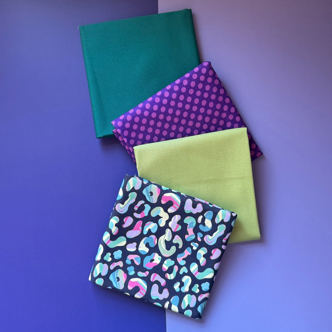 Four folded fat quarters overlapping diagonally: colourful leopard print, lime green, purple polka dots and plain teal.