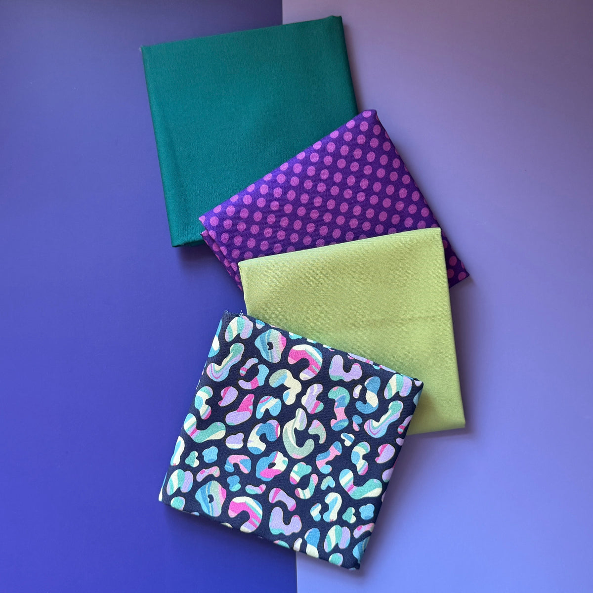 Four folded fat quarters overlapping diagonally: colourful leopard print, lime green, purple polka dots and plain teal.