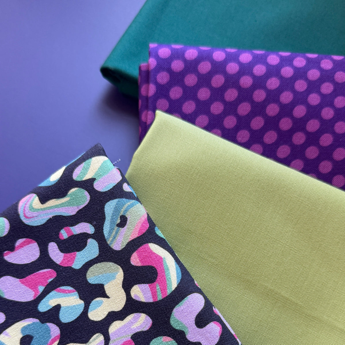 Close-up of colourful leopard-print fabric alongside lime green, purple polka dot and teal fabrics, showing their texture.
