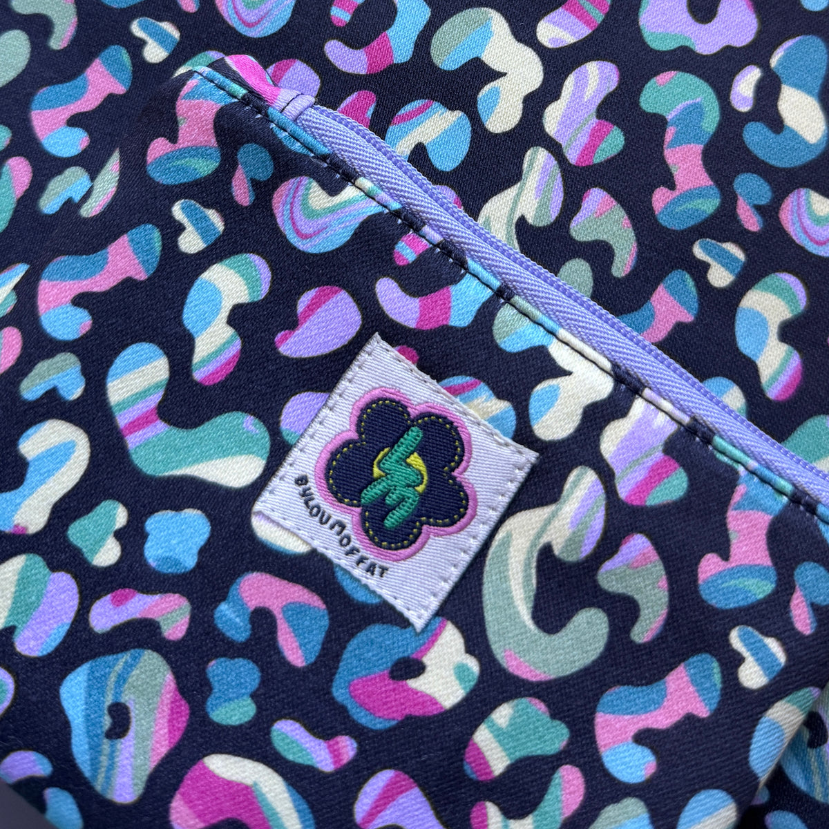 Close-up of the colourful leopard print fabric, lilac zip and stitched ByLouMoffat label.