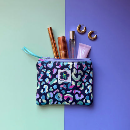 Small colourful leopard print zip pouch shown with cosmetics and gold hoop earrings. 