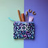 Small colourful leopard print zip pouch shown with cosmetics and gold hoop earrings. 