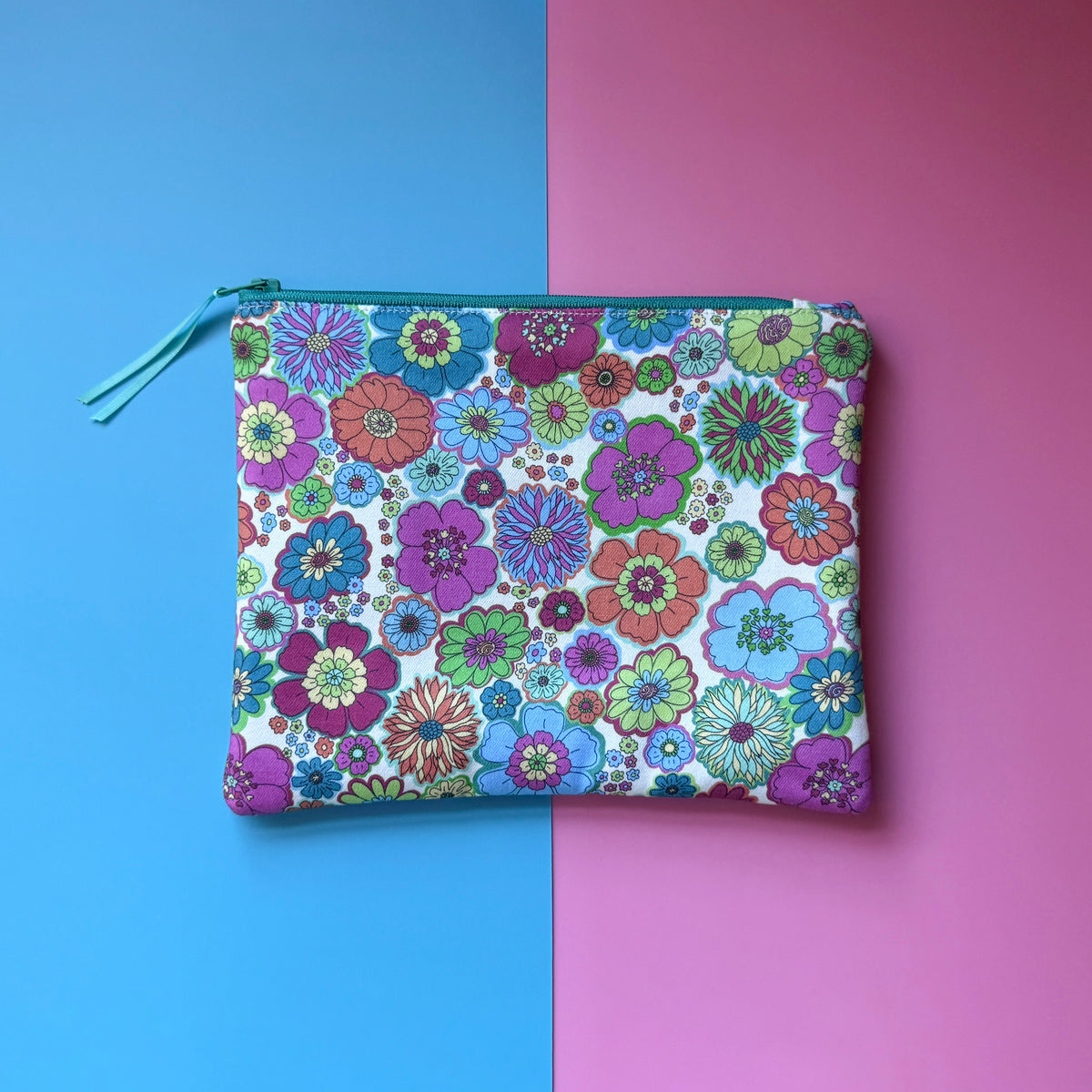Back of the medium zip pouch, showing a multicoloured 60s floral pattern and teal zip with ribbon pull.