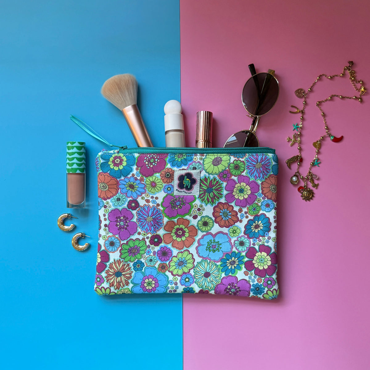 Medium size zip pouch made from a retro floral fabric inspired by the 1960s. Shown with make-up, sunglasses and jewellery.