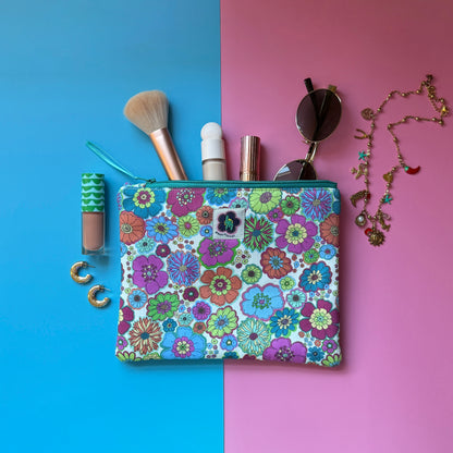 Medium size zip pouch made from a retro floral fabric inspired by the 1960s. Shown with make-up, sunglasses and jewellery.