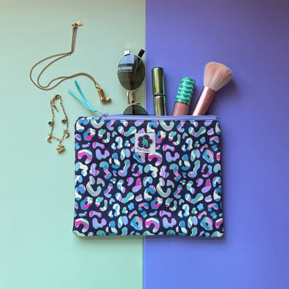 Medium leopard print zip pouch featuring colourful leopard spots on a navy background. Photographed with sunglasses, make-up, a brush and jewellery.