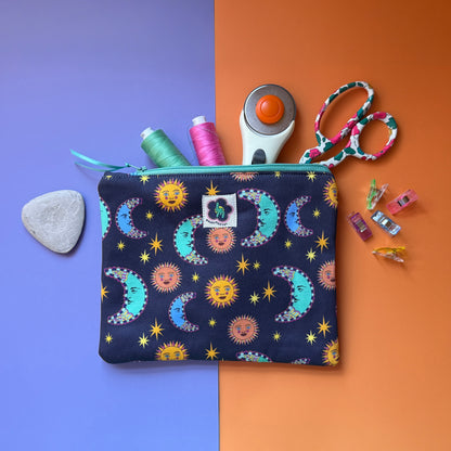 Medium navy sun and moon print pouch shown with thread, scissors, a rotary cutter and sewing clips. The fabric the pouches is made from features a navy background with teal/blue moons, orange suns and yellow stars. 