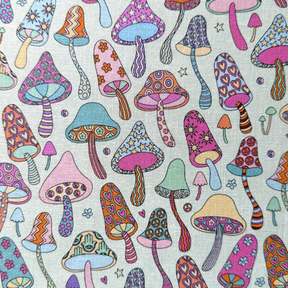 Colourful mushroom fabric laid flat, with hearts, stars, flowers, stripes and peace signs decorating the mushrooms on a pale mint green background.