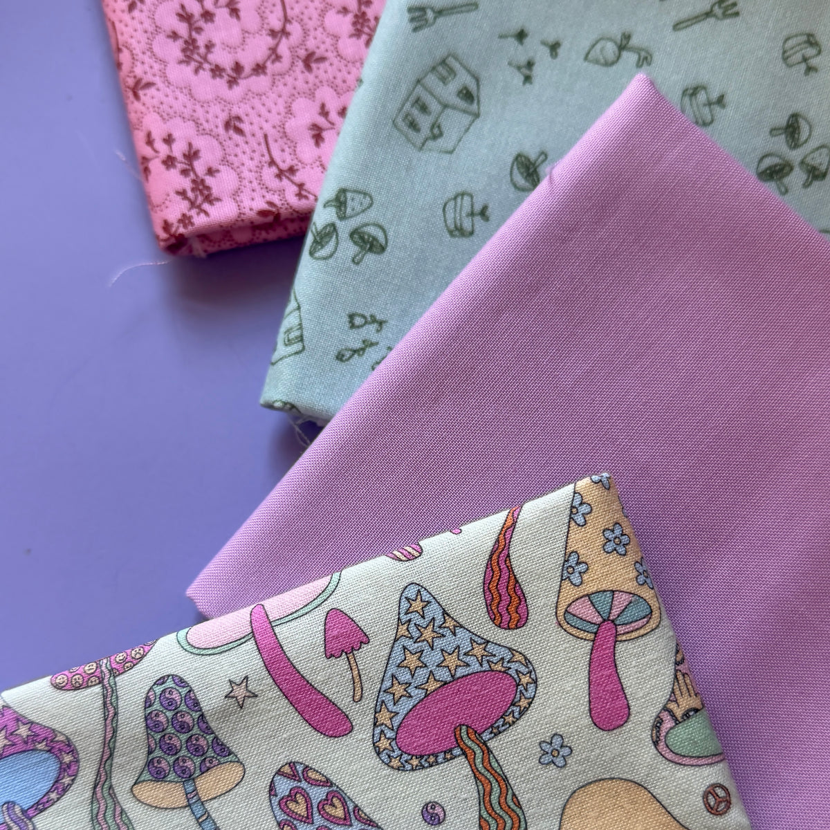 Close-up of patterned mushrooms on cream fabric alongside coordinating lilac, sage green gardening and pink floral fabrics.
