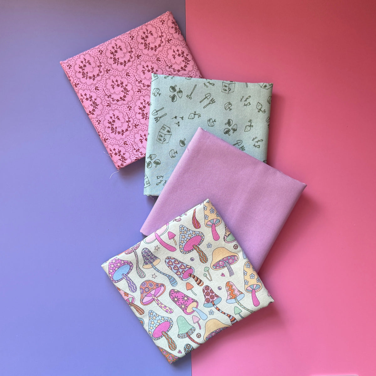 Four folded fat quarters overlapping diagonally, with colourful mushroom fabric in front of lilac, sage green gardening and pink floral paisley fabrics.