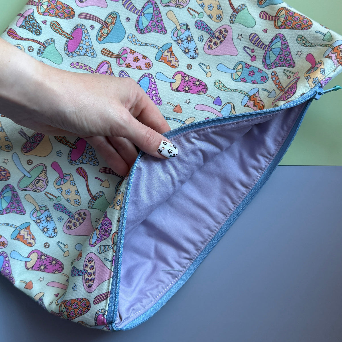 Mushroom-print pouch held open to reveal its plain lilac lining and pale blue zip.