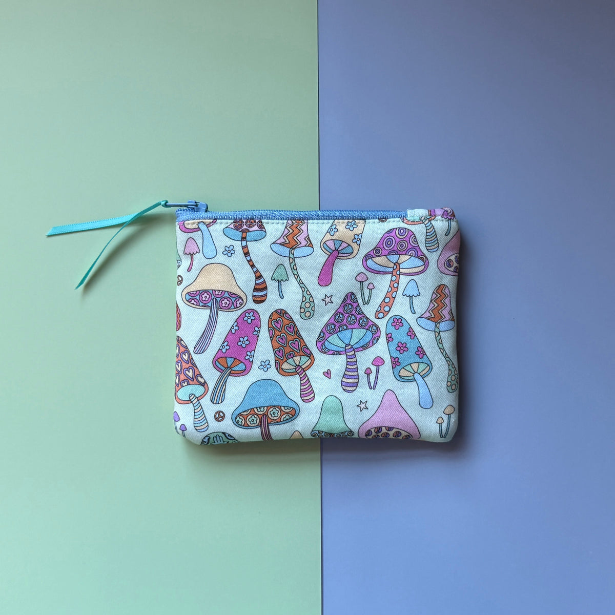 Back of the small zip pouch, showing colourful patterned mushrooms, a pale blue zip and teal ribbon pull.
