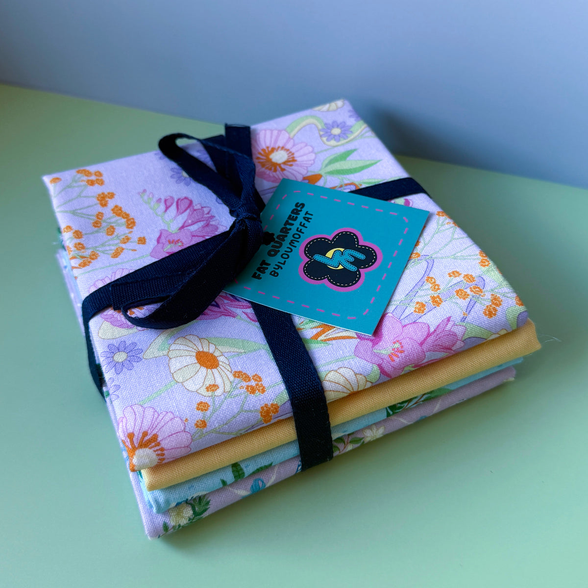 Retro Bloom fat quarter bundle stacked and tied with navy ribbon, finished with a turquoise ByLouMoffat tag.
