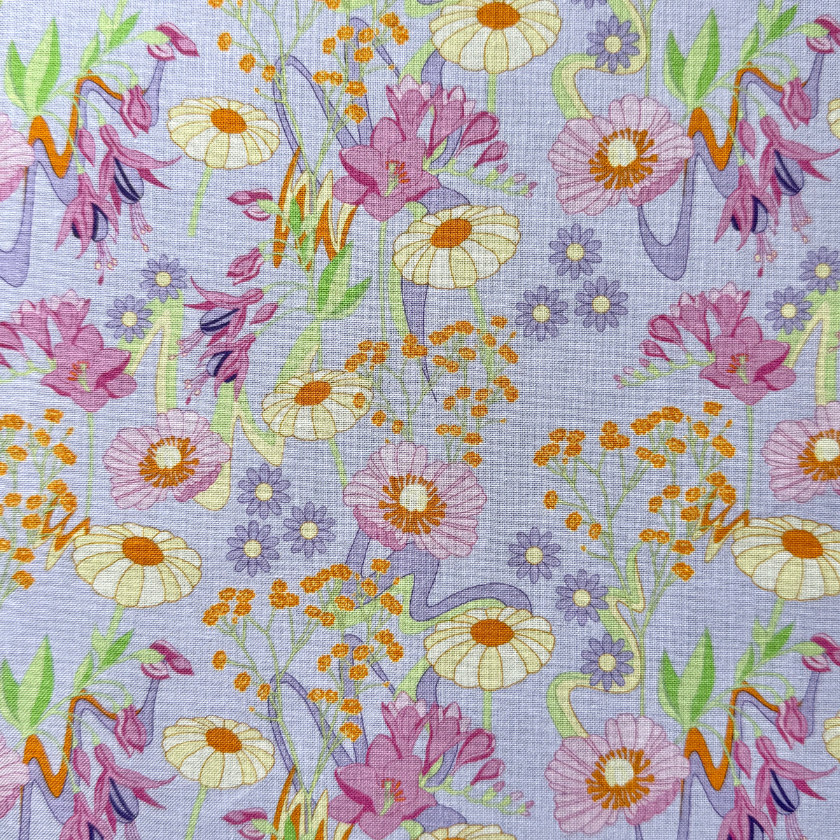 Retro Bloom fabric laid flat, featuring pink blooms, pale yellow daisies, tiny purple flowers and orange details on a pale lilac background.
